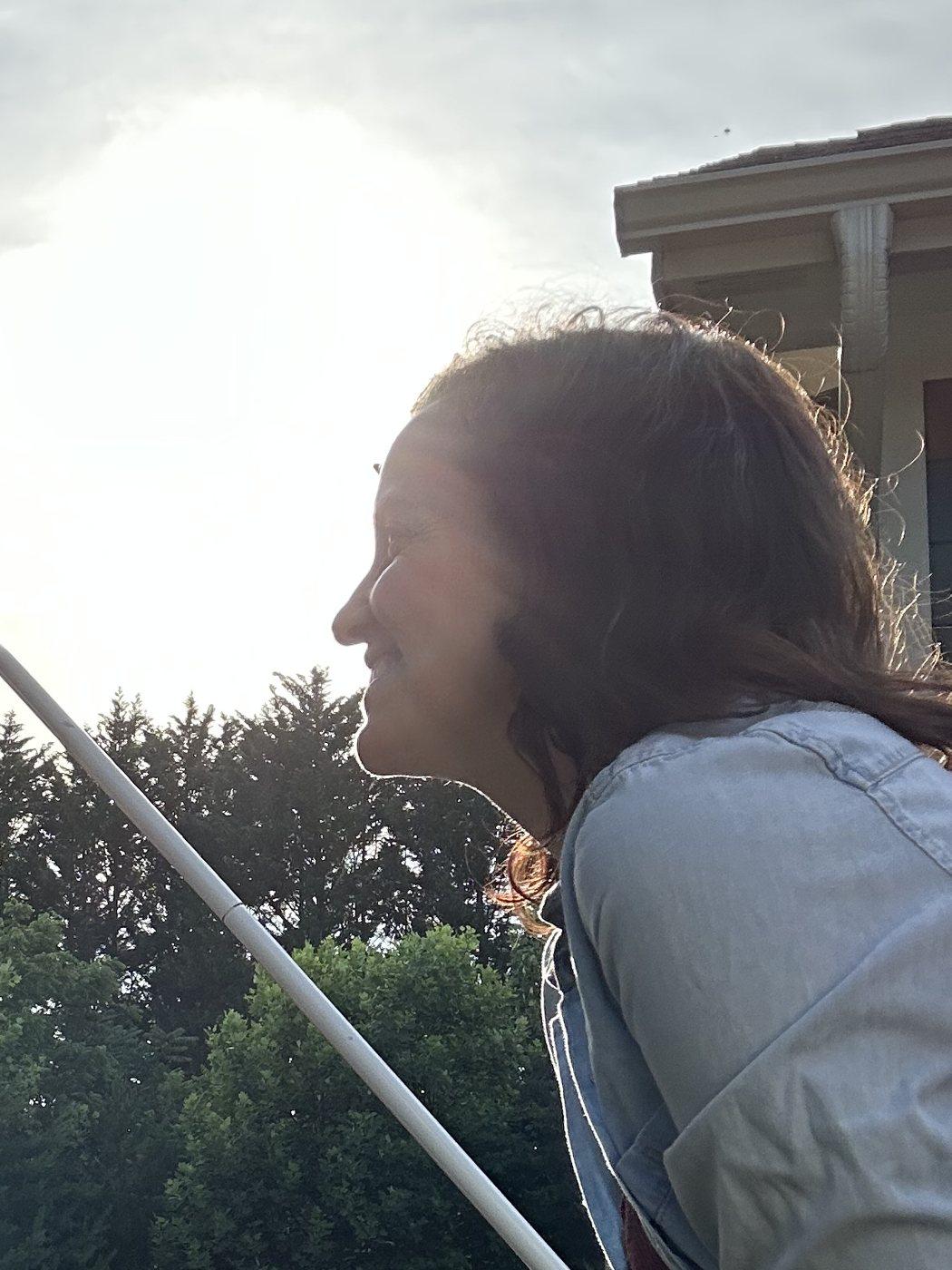 Ashley Thiesen smiling into the sunlight from a porch railing, on a trip with her daughter