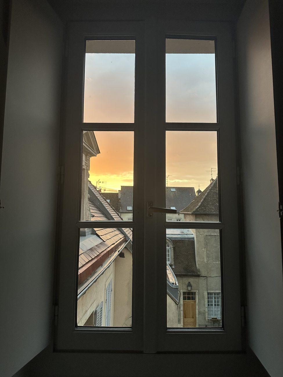 Sunset seen through a tall French window over the rooftops of Dijon