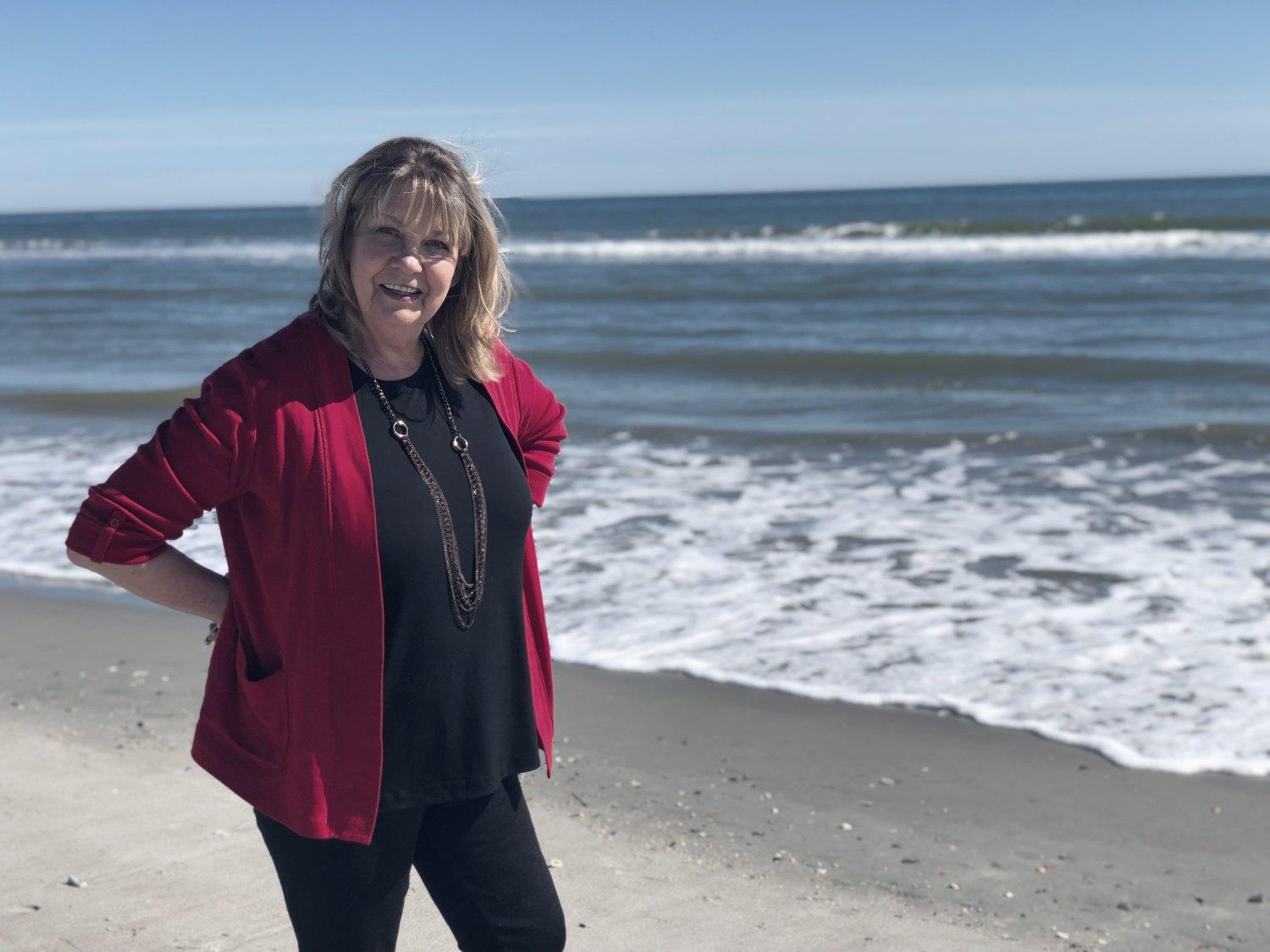 Ashley's mother standing at the ocean's edge in a red cardigan