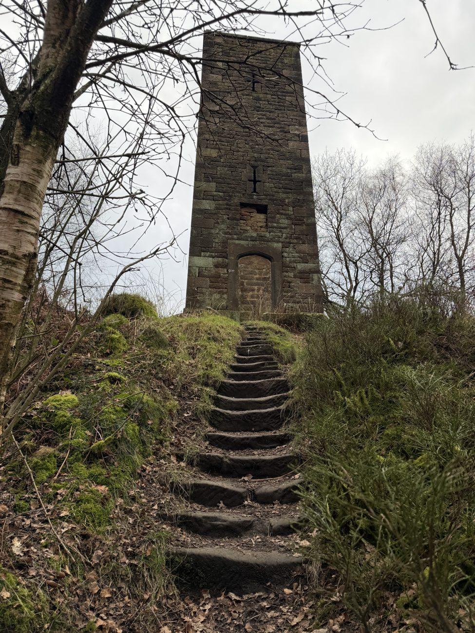 Worn stone steps leading up a mossy hill to the Reform Tower (Earl Grey Tower) on Stanton Moor in the Peak District, its doorway bricked shut