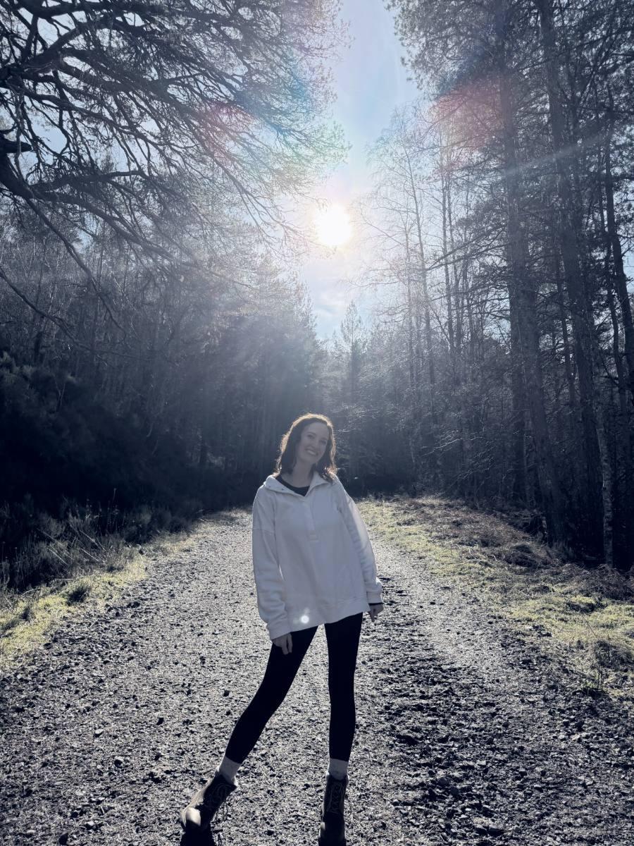 Ashley standing on a forest road with the sun breaking through the trees