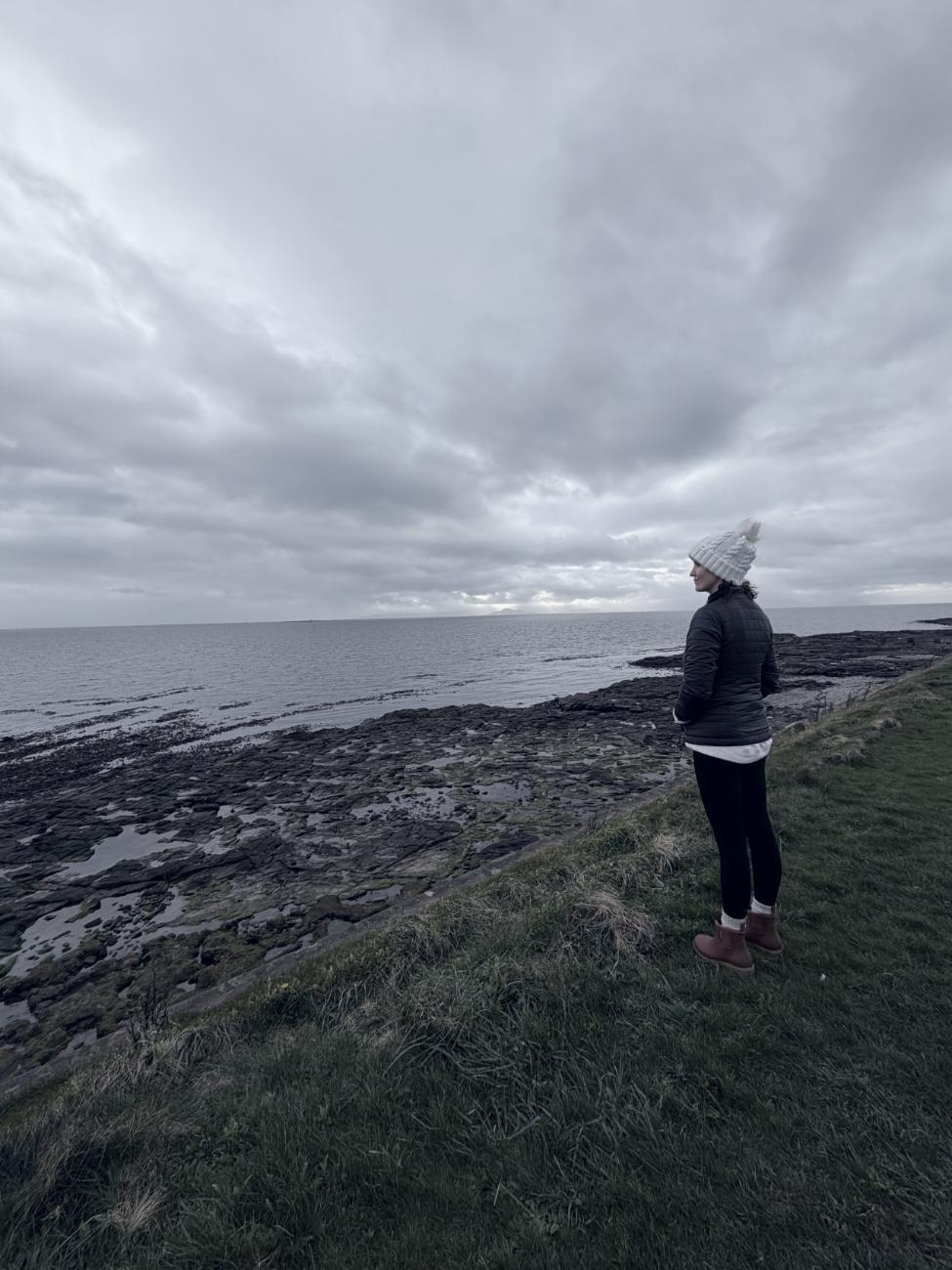 Ashley standing alone on a grassy headland looking out at a grey sea