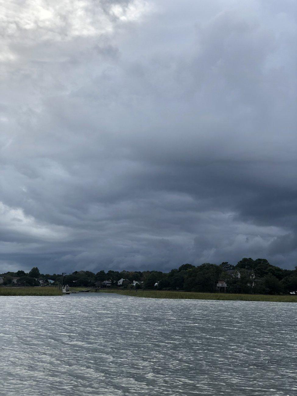 Heavy dark storm clouds hanging low over a wind-rippled tidal creek and marsh grass