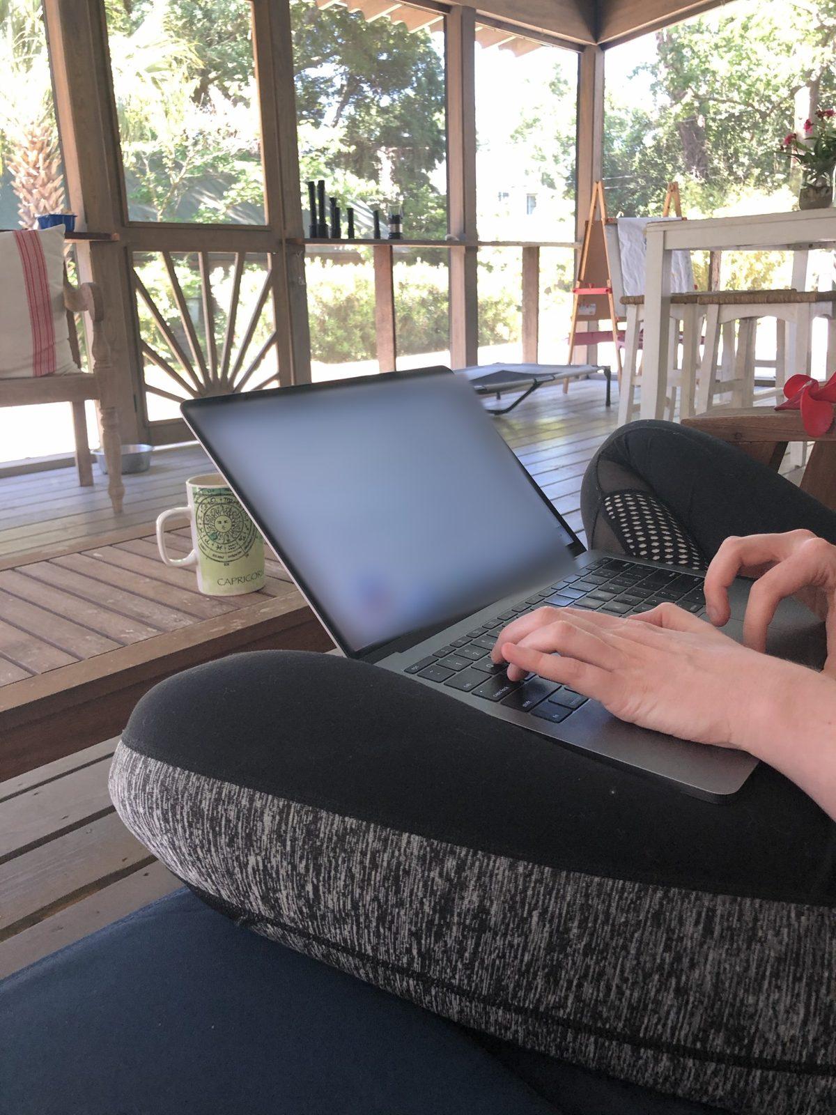 Ashley Thiesen working on her laptop on the porch at home, her daughter’s easel in the background