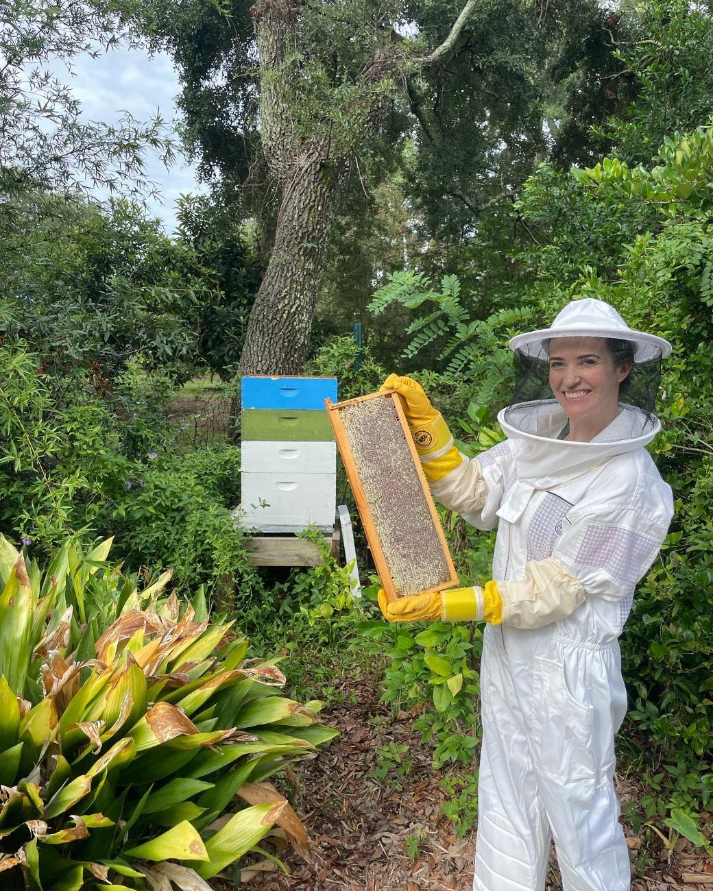 Ashley in a bee suit holding a honeycomb frame