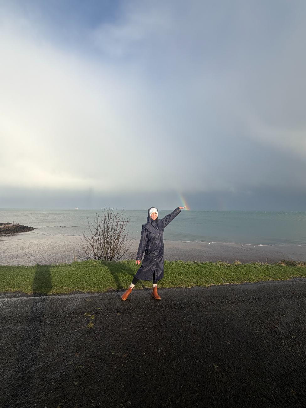 Ashley reaching toward a rainbow over the sea in Scotland