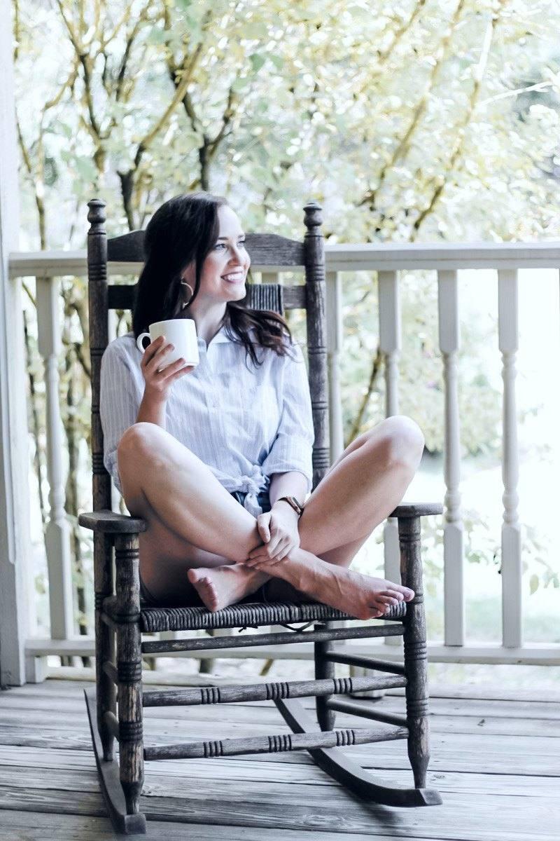 Ashley Thiesen barefoot in a porch rocking chair with coffee